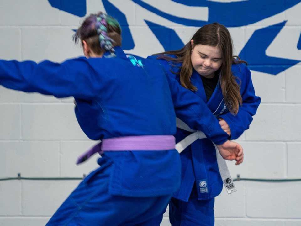 
              A student wearing a blue gi practices jiu-jitsu moves on another student.
            