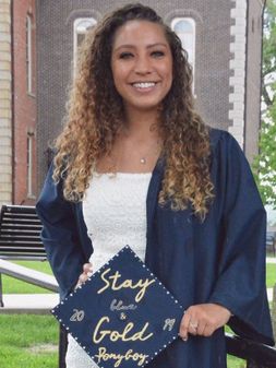 Katerina Lake posing in her graduation gown with a hat that says "Stay Blue and Gold"