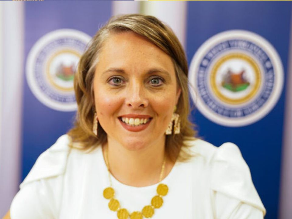 
              Award winner in front of the West Virginia State Seal, wearing a white blouse, earrings and gold necklace.
            