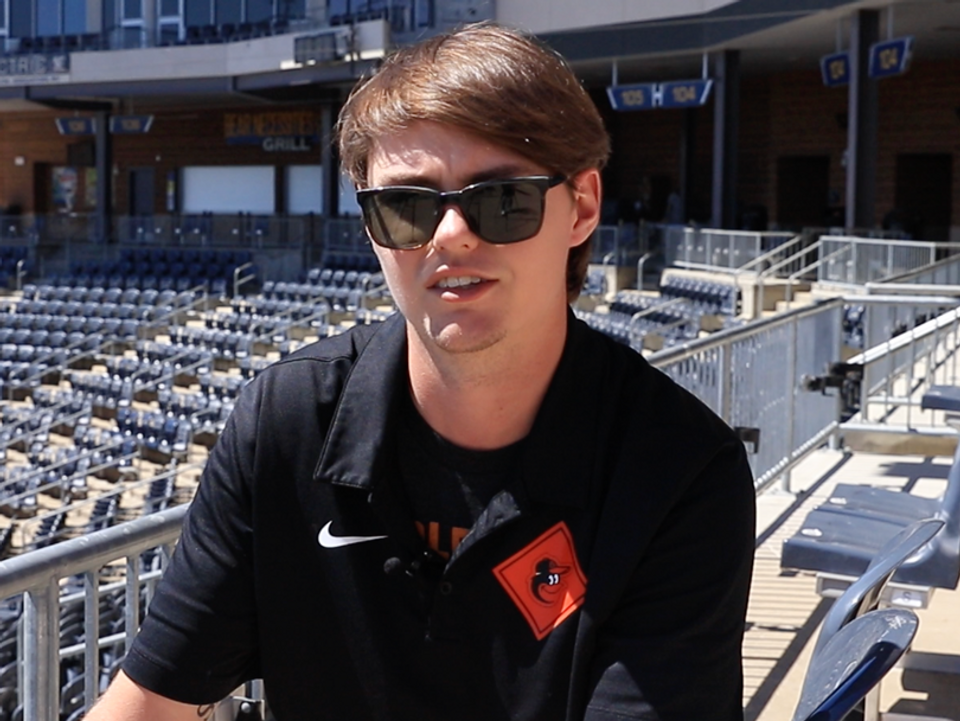 
              WVU student Samuel Gambill talking in the bleachers at Monongalia County Ballpark in a black Baltimore Orioles polo shirt and sunglasses.
            