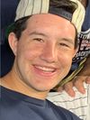 Zach Kirschner smiling, wearing dark blue t-shirt, striped baseball cap on backwards.