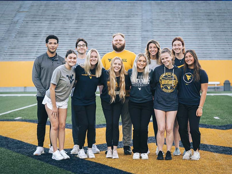 
              Health and Well-being students stand at the 50-yardline at Mountaineer Field.
            
