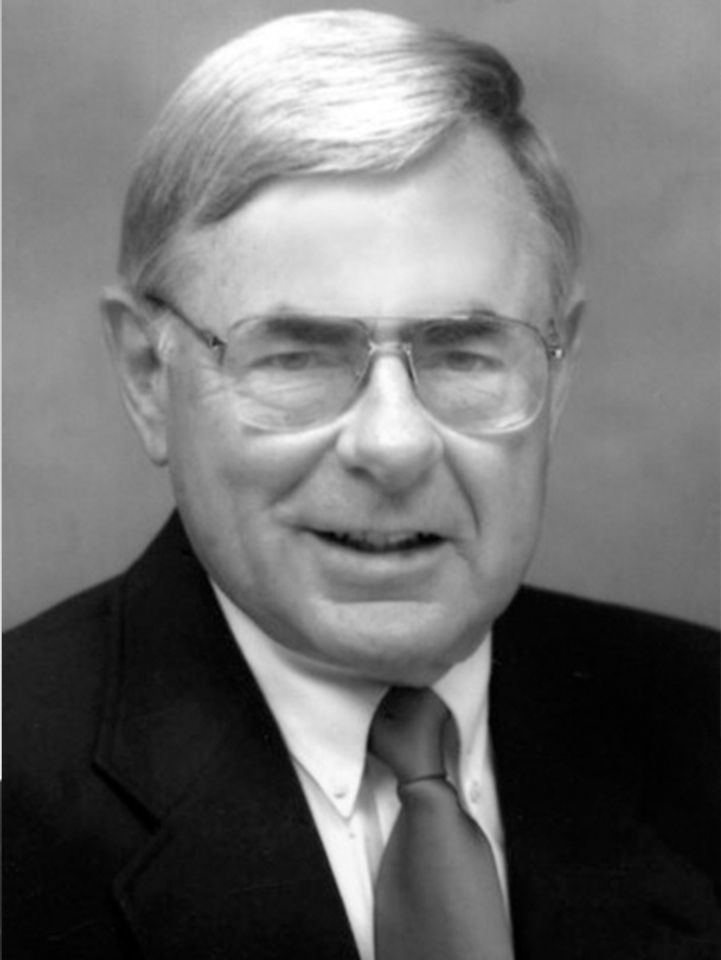 
              Former Dean Bill Douglas wearing wire framed glasses, dark suit jacket, white dress shirt and dark solid tie.
            