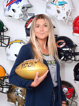 Samantha posing in front of NFL helmets holding a golden football