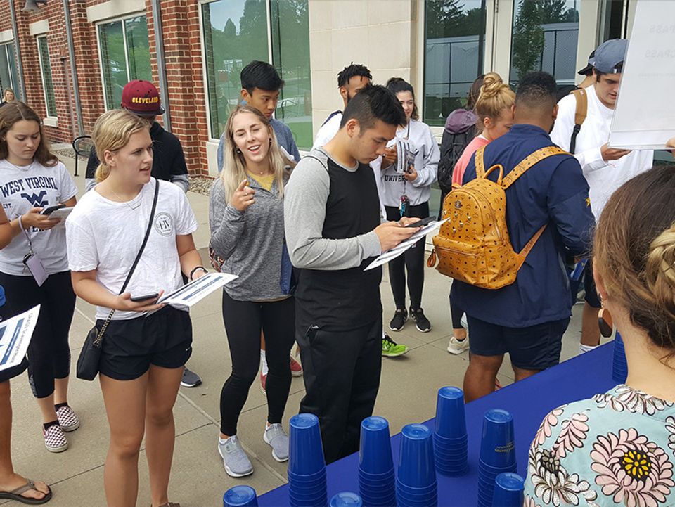 
              A group of freshman students stand outside the college building looking at their cell phones. 
            