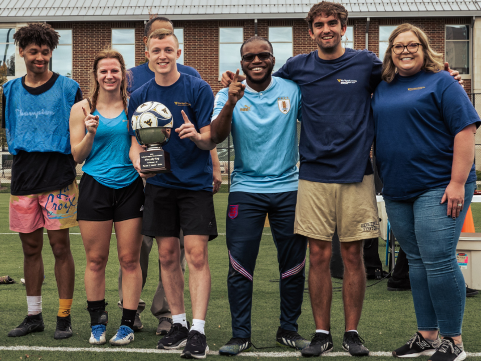 
              Several students pose outside in soccer apparel holding a soccer ball.
            