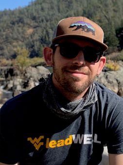 Spencer Ingels outdoors wearing a ball cap, WVU t shirt, sunglasses and bandana. 