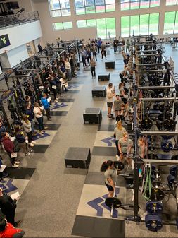 Clinic leaders are training student-athletes in large room with weight equipment while attendees watch the training session. 