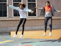 Two young girls are jumping outside on a playground