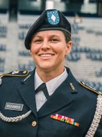 Portrait of Ashli Richards in her formal uniform holding a flag on mountaineer field